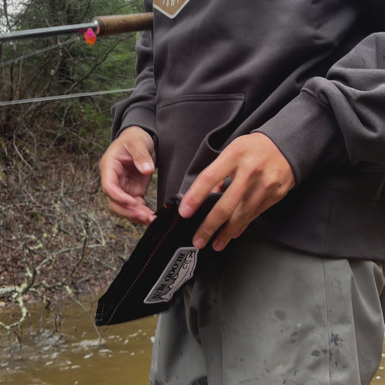 Caucasian male fishing for brook trout in a small stream in the Upper Peninsula of Michigan opening his Blood Run Fishing Black Float Fishing Wallet Bundle and removing a 5 gram camo Acorn fishing float wearing a men's coal black heavyweight fleece hoodie with the Blood Run Generator Logo on the chest and wearing a Blood Run men's brown camo knitted beanie.