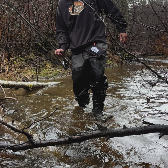 Caucasian male fishing for steelhead in a small stream in the Pacific Northwest using  a Blood Run Pinland 3 weight centerpin fishing rod, Halcyon 4.5" Centerpin reel, 15lb test clear Blood Run Float Fishing monofilament mainline, wearing a men's coal black heavyweight fleece hoodie with the Blood Run Sun Mountain Generator Logo on the chest and a brown camo knitted Blood Run Fishing beanie, carrying a Blood Run black float fishing wallet wearing simms waders.